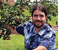 A man crouching by a red berry vine.