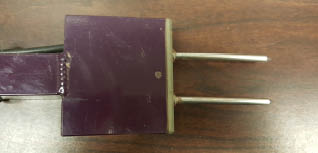 A purple, T shaped Spectrum Technologies TDR 300 sensor sitting on a wood surface.
