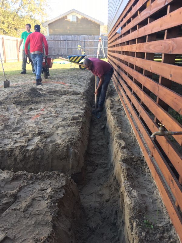Someone digs a trench with a shovel while two workers are in the background.