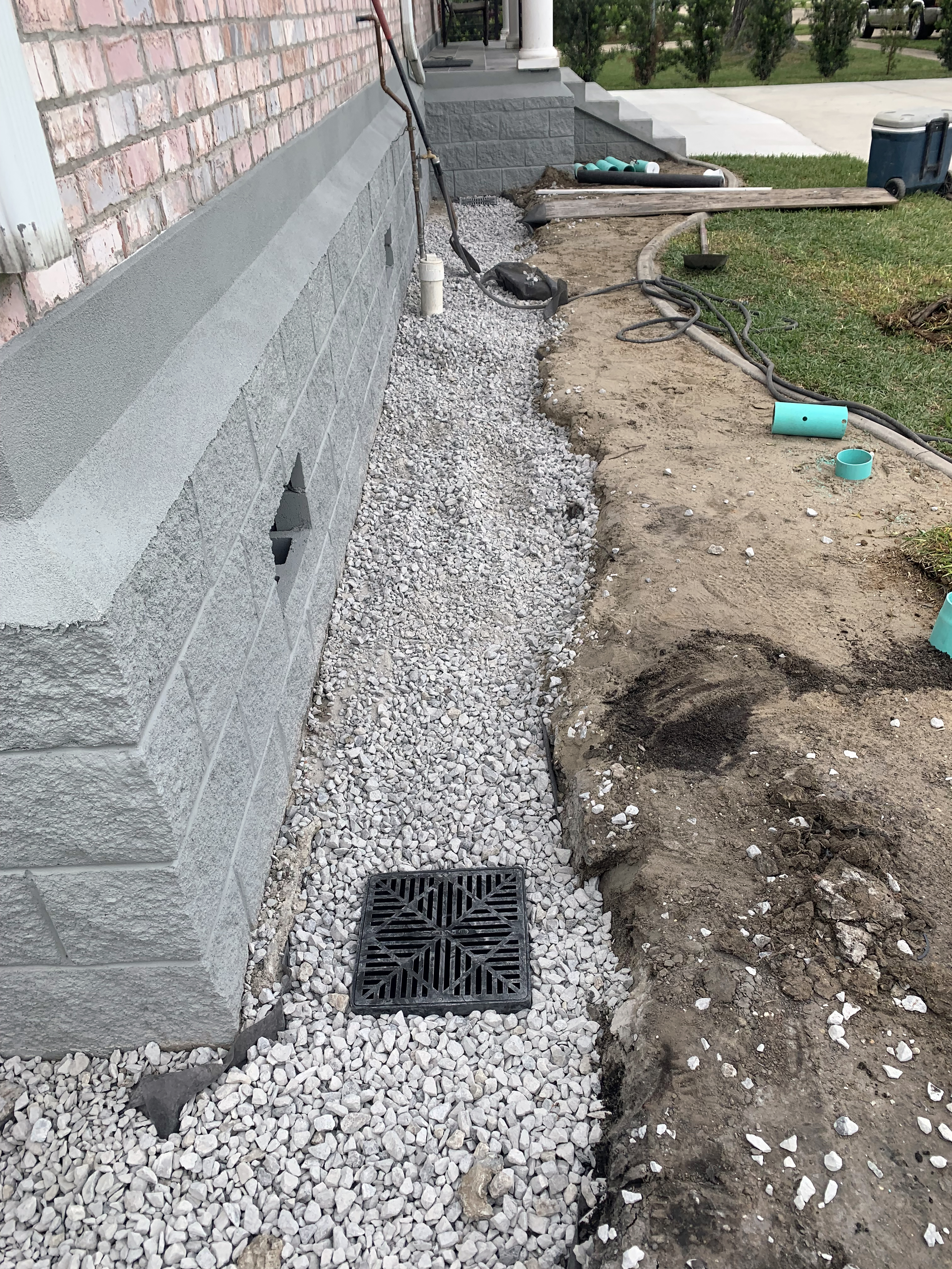 Gravel covers a trench on the side of a building.