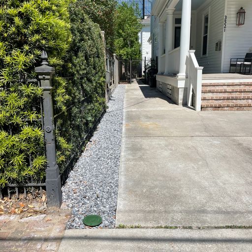 Gravel covers a trench on the side of a building.