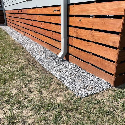Gravel covers a trench on the side of a building.