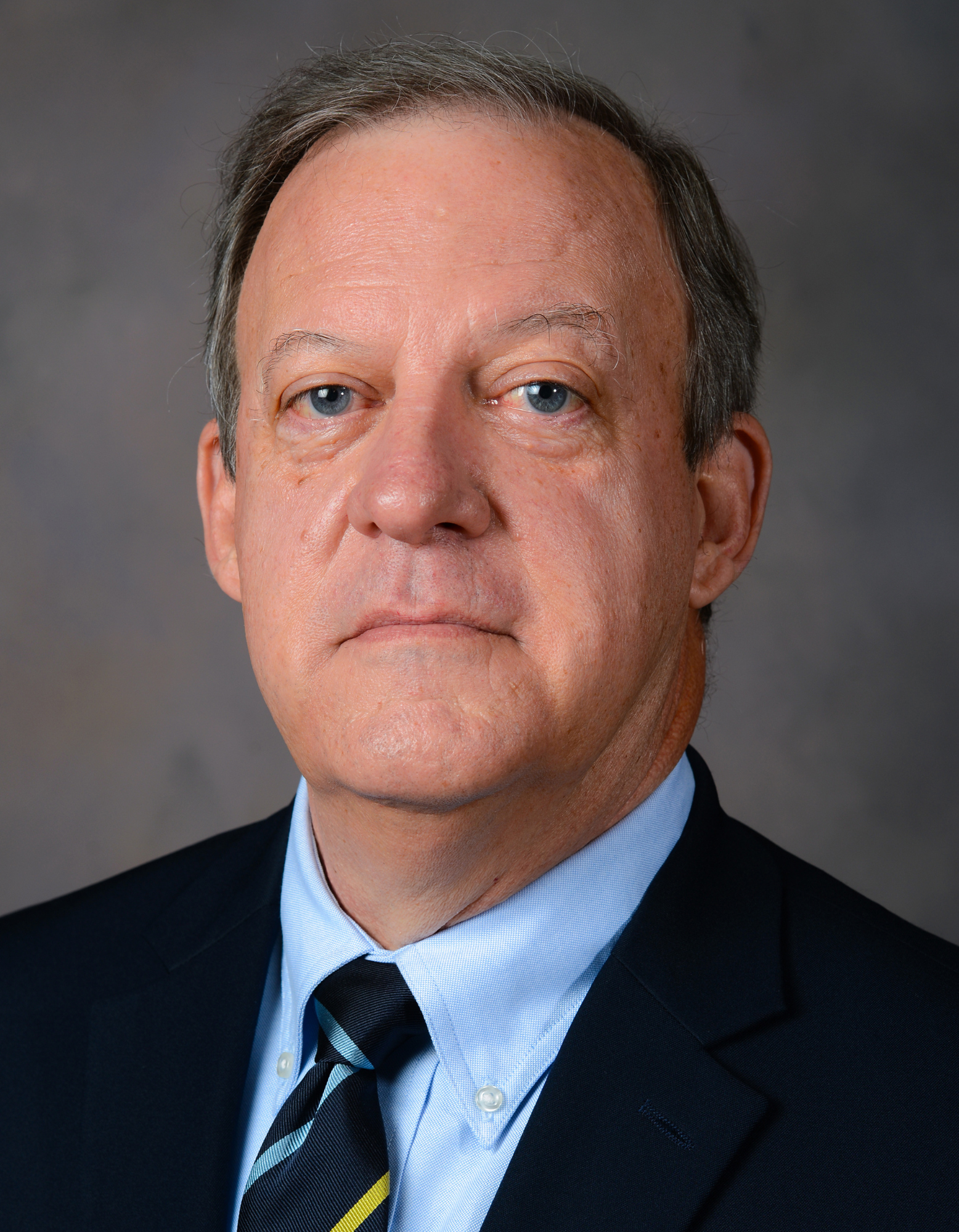Formal headshot of an individual in professional attire, posed against a neutral background. The person is smiling and dressed in business-appropriate clothing, suitable for academic, organizational, or professional representation.