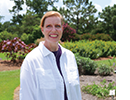 A woman poses in front of a garden. 