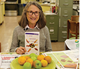 A woman wearing glasses sits at a table and poses with a book.