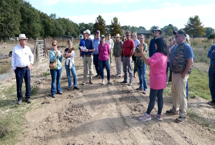 Outdoor group gathered as a speaker addresses participants in an open field.
