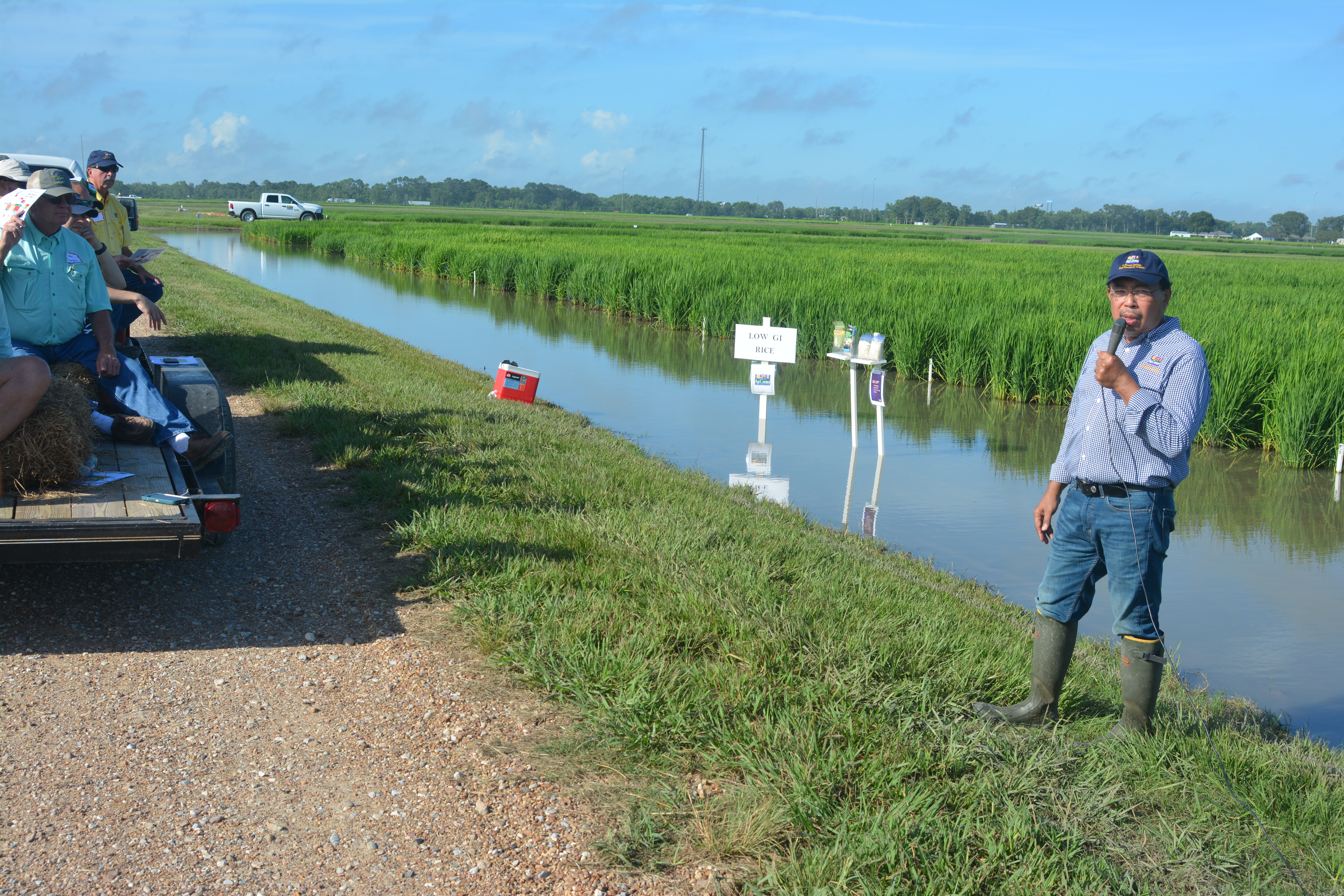 Manb standing in rice field talking to people sitting on trailer for Rice Field Day.