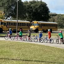 A line of kids on bicycles in front of school buses. 
