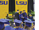 A woman poses between two men at a graduation ceremony.