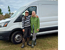 Two women stand arm in arm in front of a van.