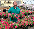 A man stands in front of plants with pink flowers.