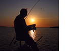 A man with a fishing pole is shown in silhouette in front of a sunset.