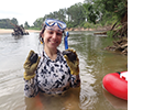 A woman stands in a river and holds two mussels.