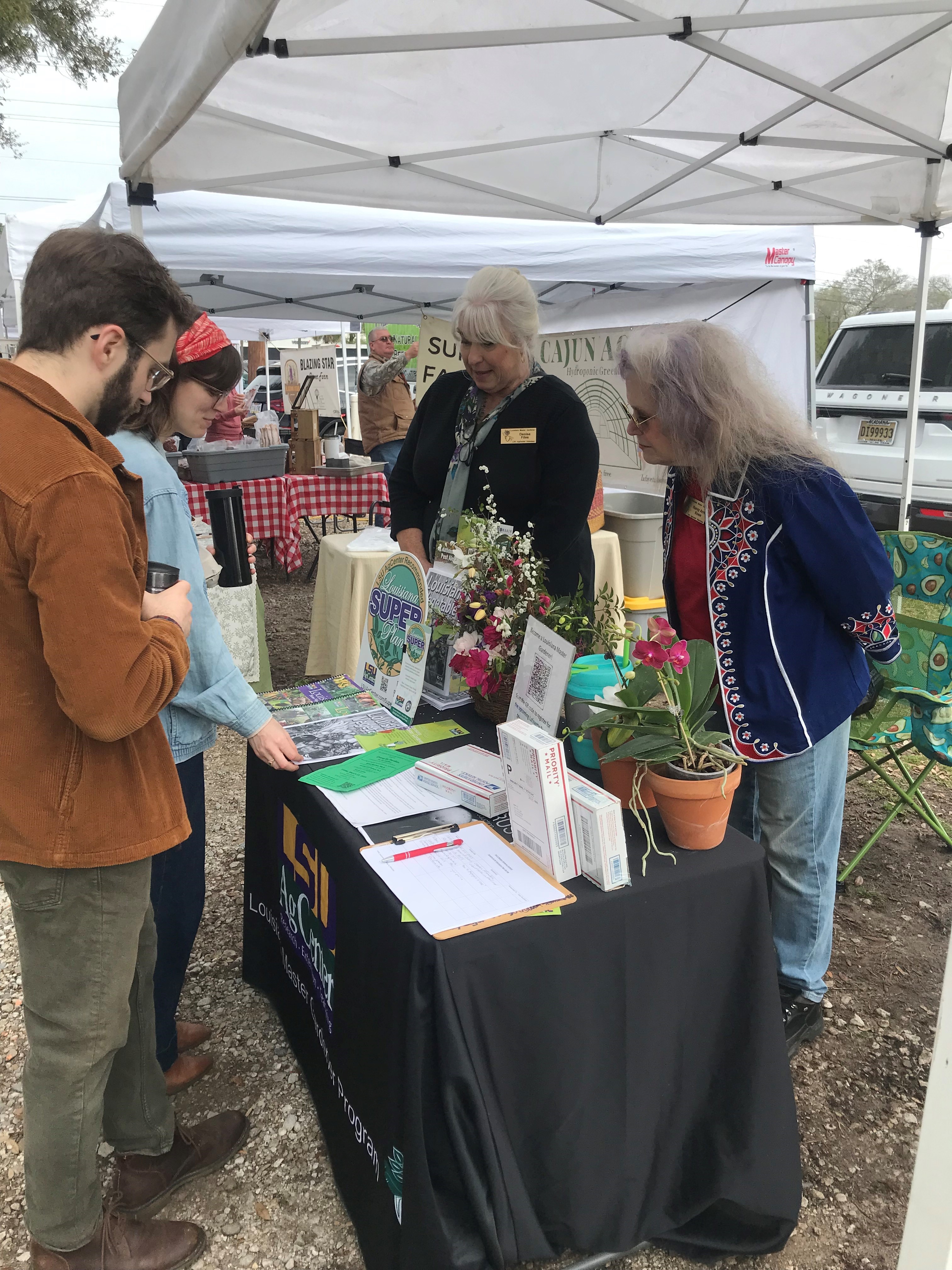 Two volunteers answering questions about Louisiana Super Plants at a booth set up at a local farmer's market.