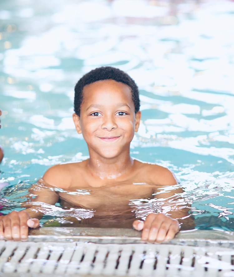 A boy smiles while stopping at the edge of a swimming pool.