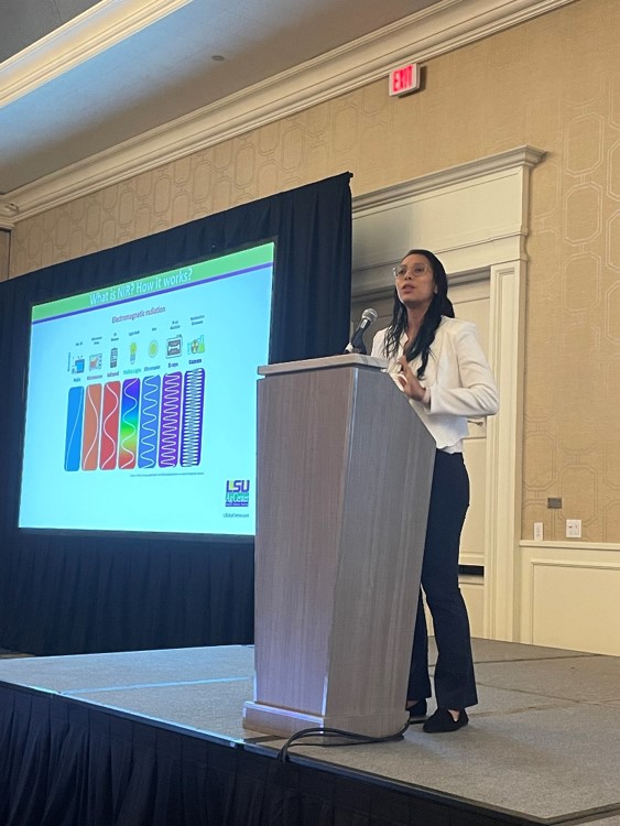 Woman standing on a platform giving an oral presentation.