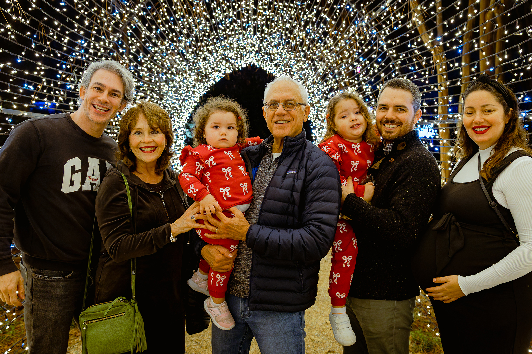Group photo beneath a tunnel of holiday lights at an outdoor seasonal display. 